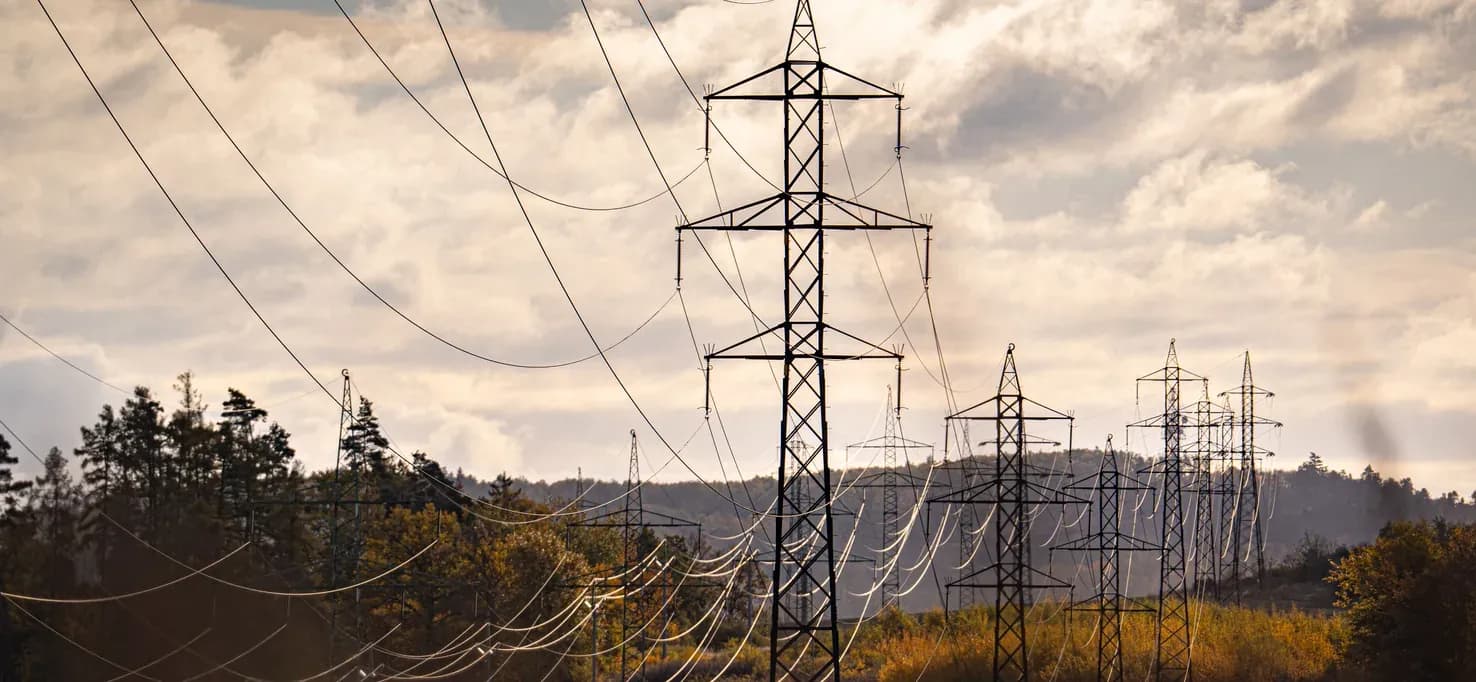High-voltage power lines crossing open countryside under a cloudy sky