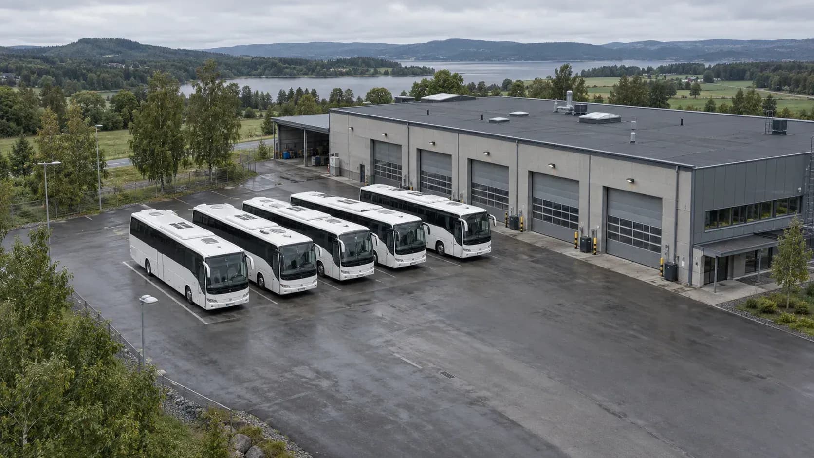 White coaches parked outside a bus depot and workshop beside a lake